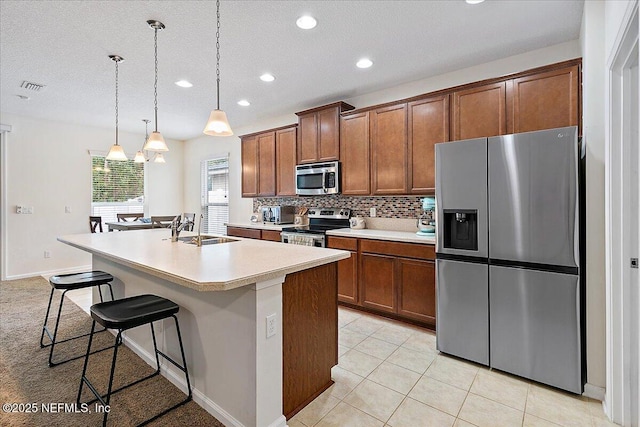 kitchen featuring sink, pendant lighting, a center island with sink, a breakfast bar, and appliances with stainless steel finishes