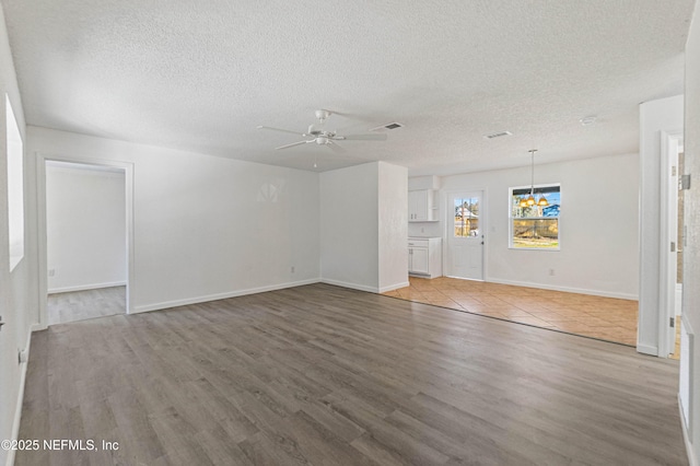 unfurnished living room featuring hardwood / wood-style flooring, ceiling fan with notable chandelier, and a textured ceiling