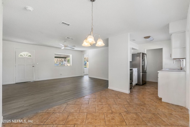 unfurnished living room with sink, ceiling fan with notable chandelier, light hardwood / wood-style floors, and a textured ceiling