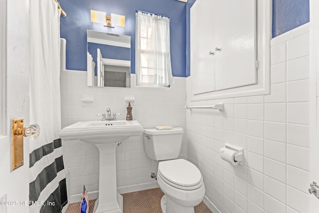 bathroom featuring tile patterned floors, toilet, and tile walls