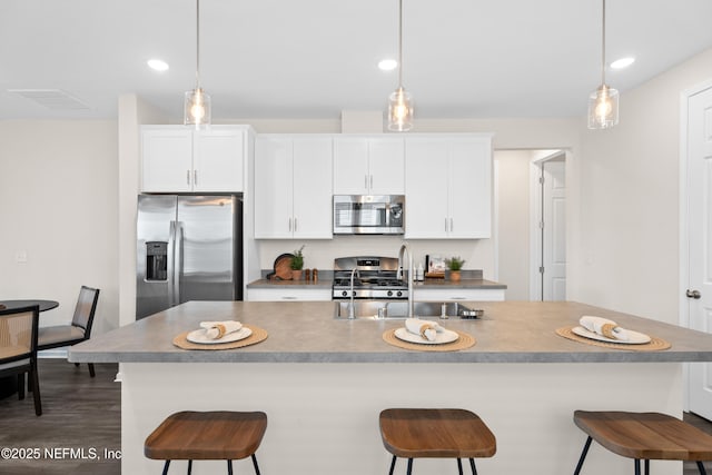 kitchen featuring white cabinetry, appliances with stainless steel finishes, a center island with sink, and hanging light fixtures