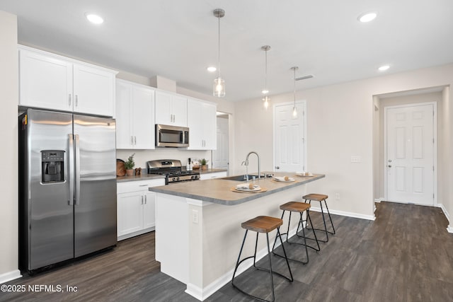 kitchen with white cabinets, appliances with stainless steel finishes, decorative light fixtures, an island with sink, and sink