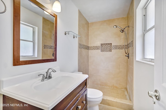 bathroom featuring toilet, tiled shower, and vanity