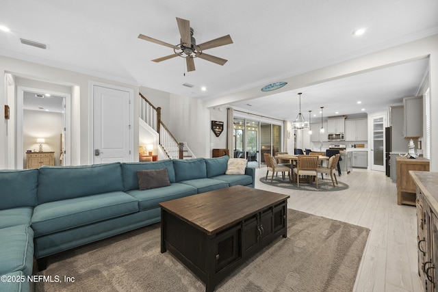 living room featuring light hardwood / wood-style floors, ornamental molding, and ceiling fan with notable chandelier