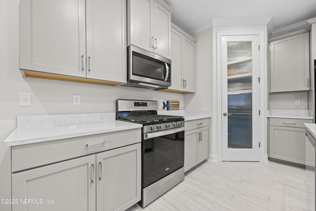 kitchen featuring light stone countertops, appliances with stainless steel finishes, light hardwood / wood-style flooring, and crown molding