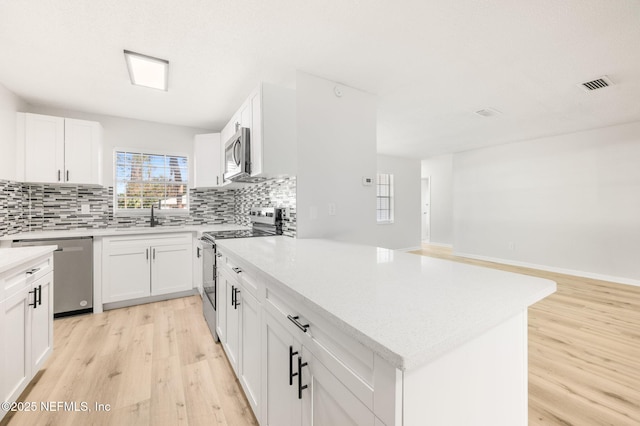 kitchen featuring white cabinets, appliances with stainless steel finishes, sink, backsplash, and light hardwood / wood-style flooring