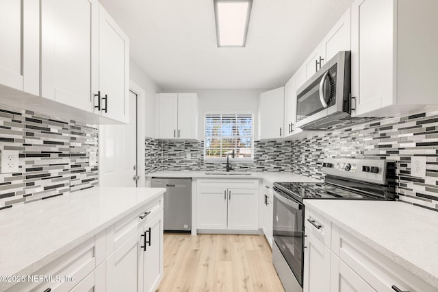 kitchen featuring white cabinetry, appliances with stainless steel finishes, decorative backsplash, light wood-type flooring, and sink