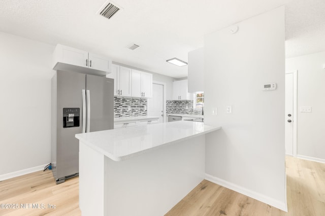 kitchen with kitchen peninsula, stainless steel refrigerator with ice dispenser, backsplash, light wood-type flooring, and white cabinets