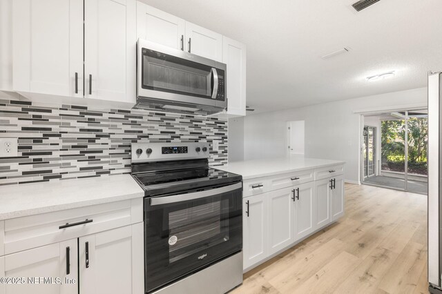 kitchen with light wood-type flooring, white cabinets, decorative backsplash, and appliances with stainless steel finishes