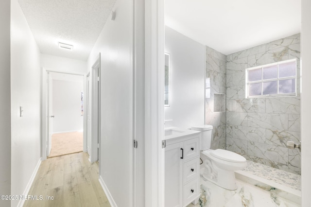 bathroom with toilet, vanity, tiled shower, wood-type flooring, and a textured ceiling