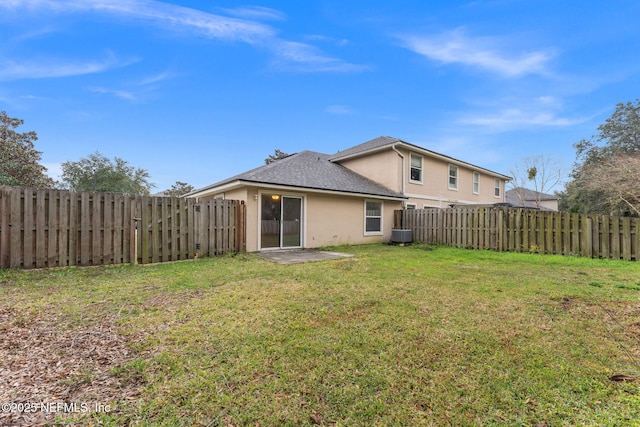 rear view of house with stucco siding, a fenced backyard, and a yard