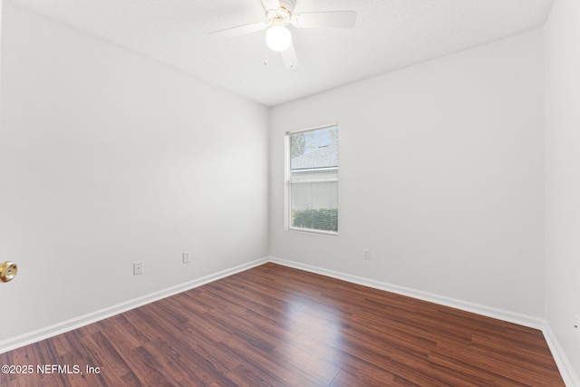 empty room with dark wood finished floors, a ceiling fan, and baseboards