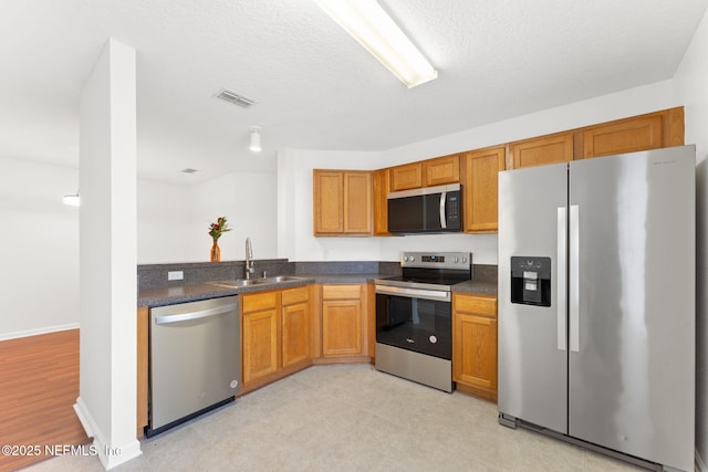 kitchen with stainless steel appliances, dark countertops, visible vents, and a sink