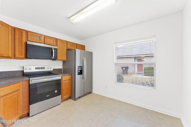 kitchen featuring stainless steel appliances, dark countertops, brown cabinets, and baseboards