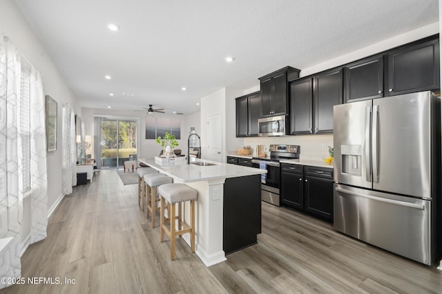 kitchen featuring a kitchen bar, appliances with stainless steel finishes, a kitchen island with sink, light hardwood / wood-style flooring, and sink