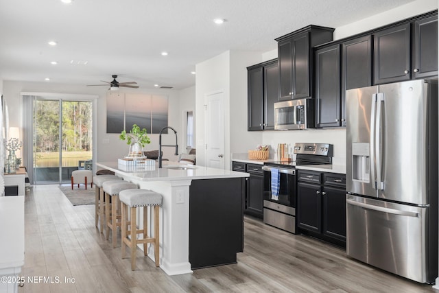 kitchen featuring stainless steel appliances, sink, a kitchen breakfast bar, a kitchen island with sink, and light hardwood / wood-style flooring