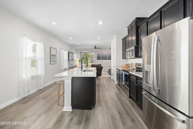 kitchen with sink, light wood-type flooring, an island with sink, a breakfast bar area, and stainless steel appliances