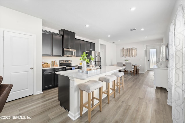 kitchen with light hardwood / wood-style floors, a kitchen bar, sink, an island with sink, and stainless steel appliances