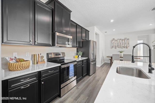 kitchen featuring light stone countertops, a textured ceiling, appliances with stainless steel finishes, light hardwood / wood-style floors, and sink