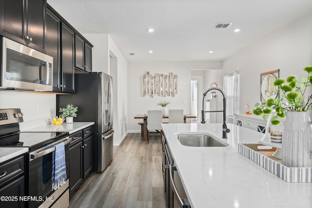 kitchen featuring light stone countertops, a textured ceiling, stainless steel appliances, sink, and light wood-type flooring