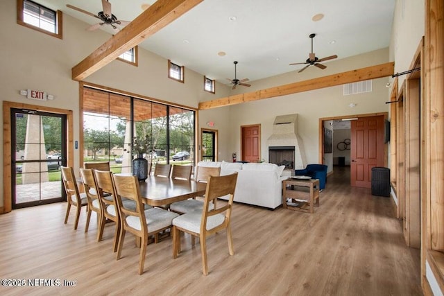 dining space featuring a towering ceiling, beamed ceiling, and light hardwood / wood-style flooring