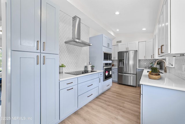 kitchen featuring stainless steel appliances, sink, white cabinetry, wall chimney range hood, and lofted ceiling