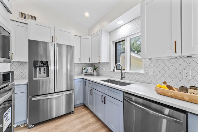 kitchen with white cabinetry, appliances with stainless steel finishes, vaulted ceiling, and sink