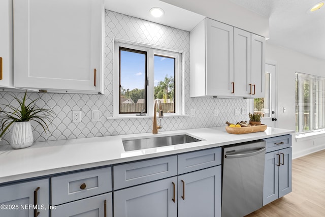 kitchen with sink, light hardwood / wood-style floors, stainless steel dishwasher, decorative backsplash, and gray cabinets