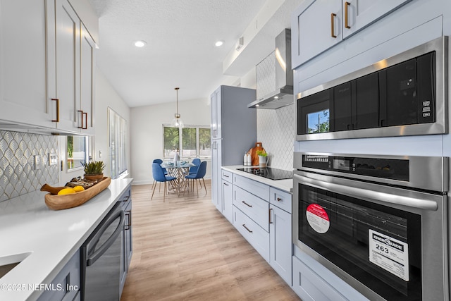 kitchen with vaulted ceiling, wall chimney exhaust hood, hanging light fixtures, backsplash, and appliances with stainless steel finishes