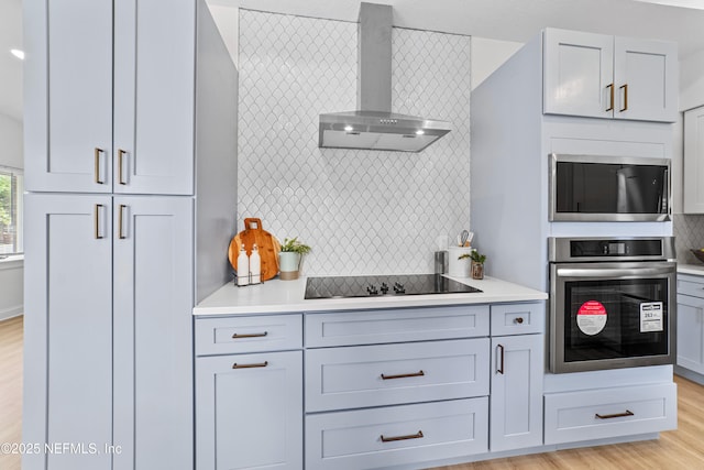 kitchen with wall chimney exhaust hood, light hardwood / wood-style floors, tasteful backsplash, and appliances with stainless steel finishes