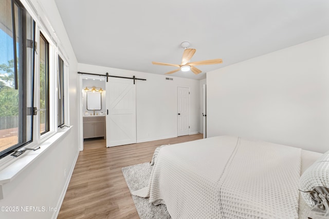 bedroom with hardwood / wood-style floors, ceiling fan, a barn door, and connected bathroom