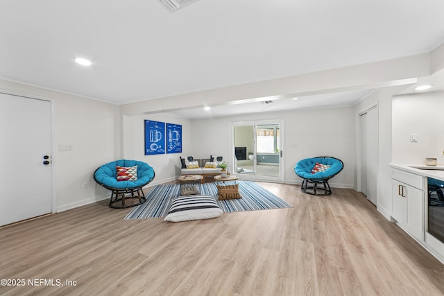 sitting room featuring sink, light wood-type flooring, and crown molding