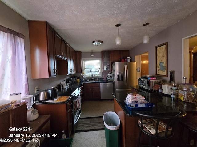 kitchen with decorative light fixtures, sink, a textured ceiling, and stainless steel appliances