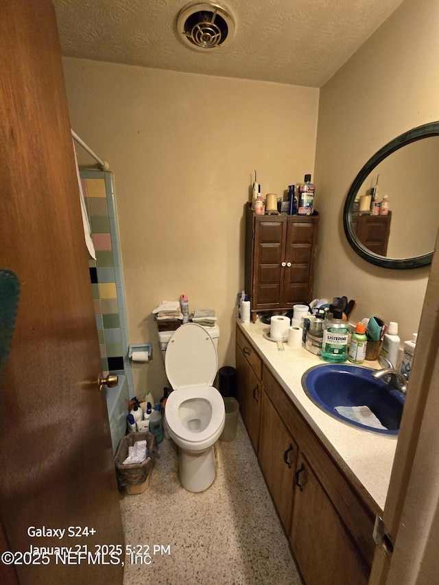 bathroom featuring a textured ceiling, toilet, walk in shower, and vanity