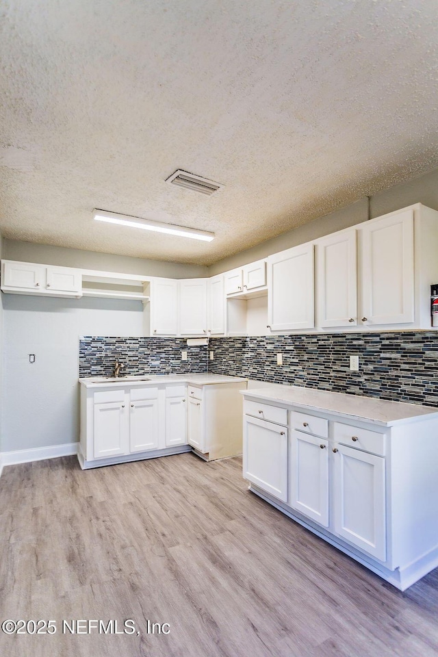 kitchen featuring backsplash, sink, white cabinets, and light wood-type flooring