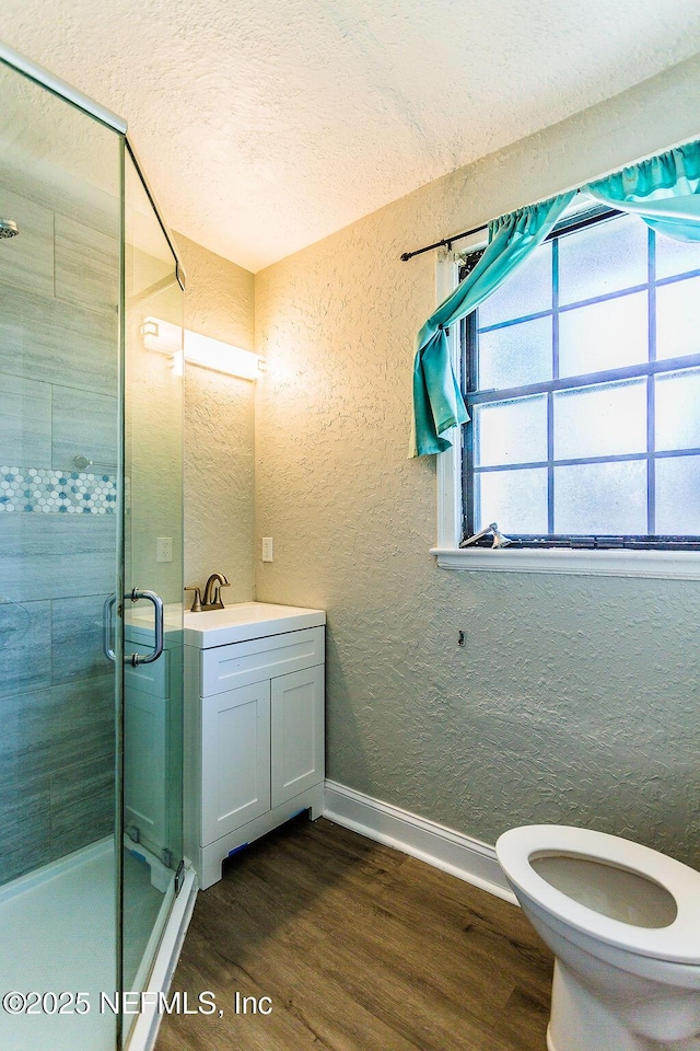 bathroom featuring hardwood / wood-style floors, a shower with shower door, vanity, toilet, and a textured ceiling