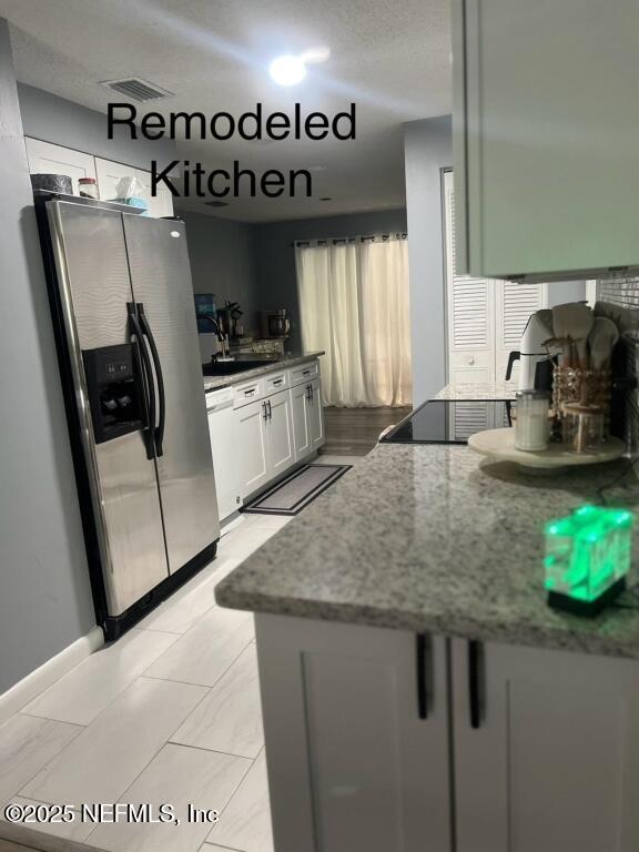 kitchen with kitchen peninsula, stainless steel refrigerator with ice dispenser, sink, white cabinets, and dark stone counters