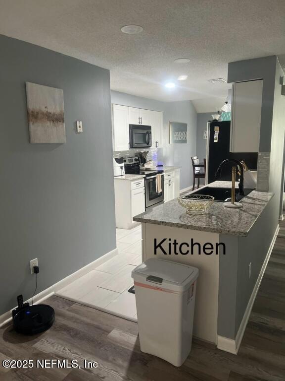 kitchen featuring light stone countertops, white cabinets, black appliances, sink, and kitchen peninsula