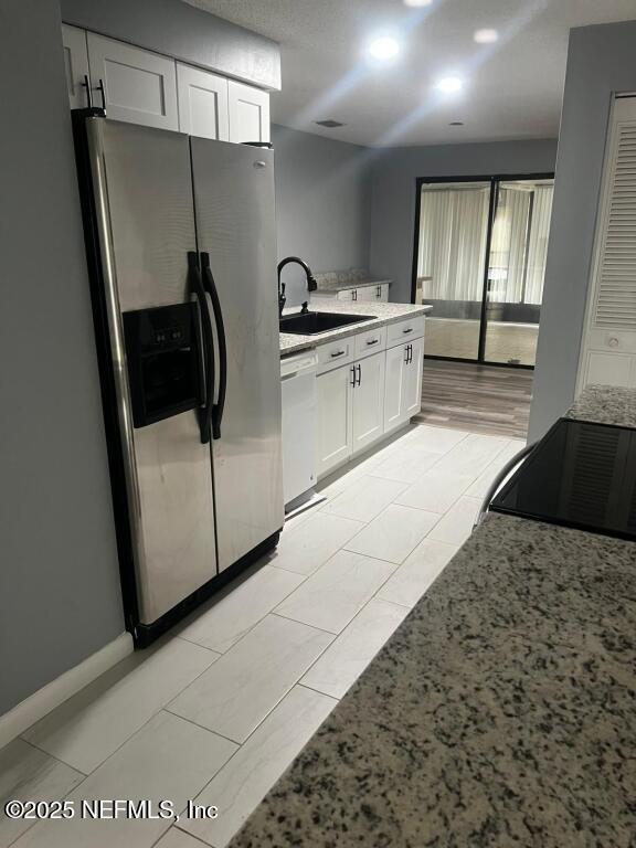 kitchen featuring sink, white dishwasher, white cabinetry, stainless steel fridge, and range