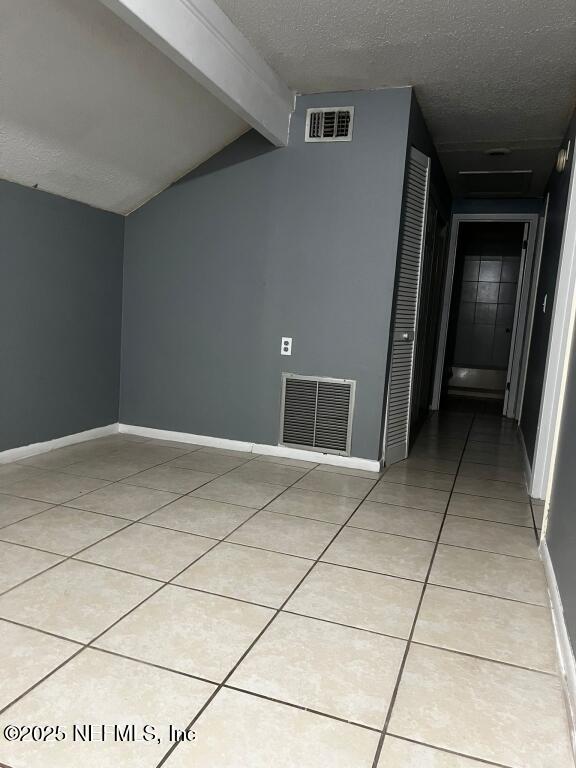 interior space featuring a textured ceiling, light tile patterned floors, and lofted ceiling with beams