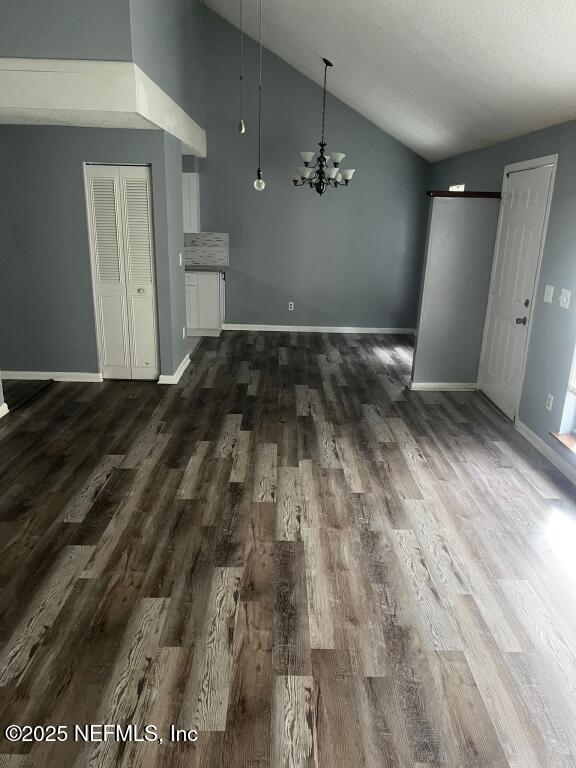 unfurnished dining area featuring dark wood-type flooring, a textured ceiling, an inviting chandelier, and vaulted ceiling