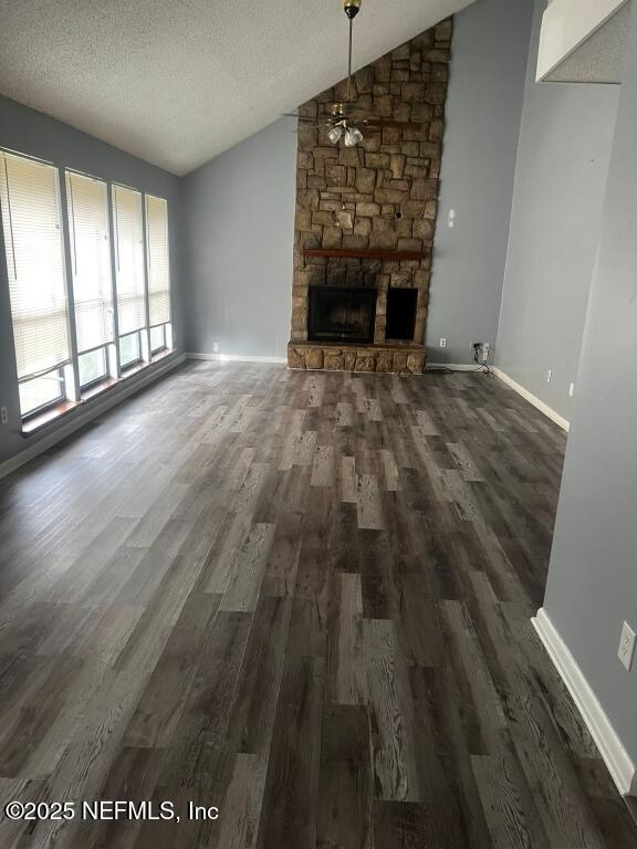 unfurnished living room featuring a textured ceiling, lofted ceiling, dark wood-type flooring, a stone fireplace, and ceiling fan