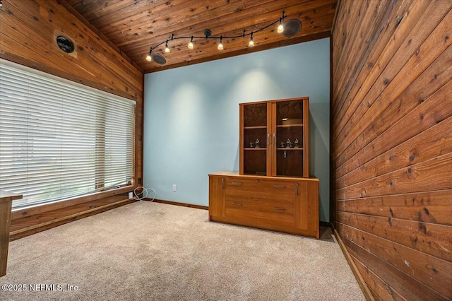 carpeted empty room featuring track lighting, wooden ceiling, vaulted ceiling, and wood walls