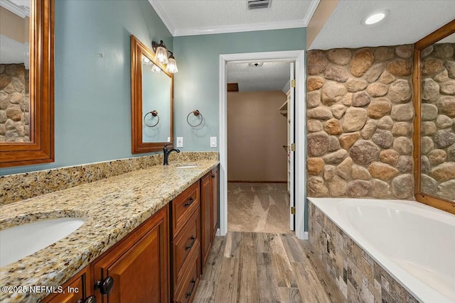 bathroom featuring wood-type flooring, vanity, ornamental molding, a relaxing tiled tub, and a textured ceiling