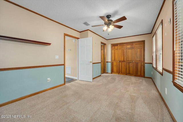 unfurnished bedroom with ceiling fan, ornamental molding, a closet, and light carpet