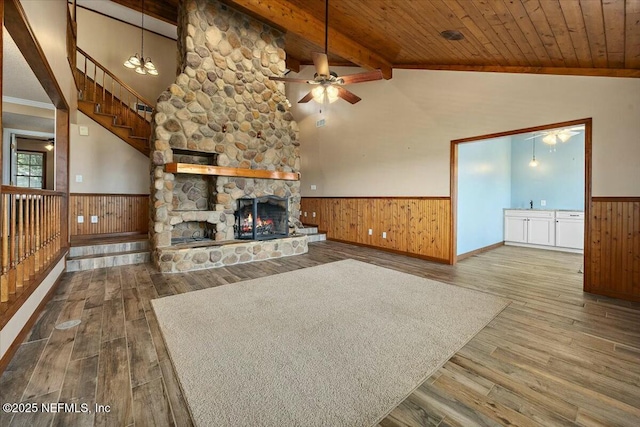 unfurnished living room with a fireplace, wood-type flooring, vaulted ceiling with beams, ceiling fan, and wooden ceiling