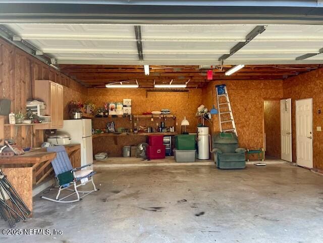 garage featuring water heater, white refrigerator, and a workshop area