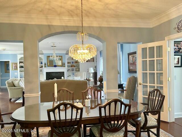 dining area with wood-type flooring, built in features, ornamental molding, and an inviting chandelier