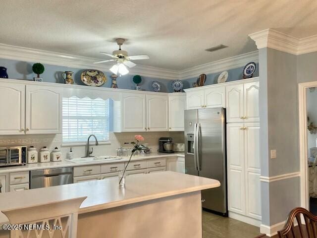 kitchen with white cabinets, appliances with stainless steel finishes, sink, ceiling fan, and crown molding