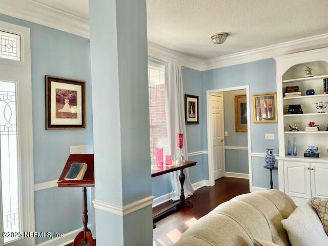 living area with a textured ceiling, crown molding, dark hardwood / wood-style floors, and built in shelves